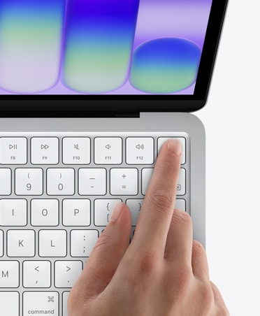 Sidabro spalvos „MacBook Neo“, žmogaus pirštas ant „Touch ID“ jutiklio klaviatūros dešiniame viršutiniame kampe