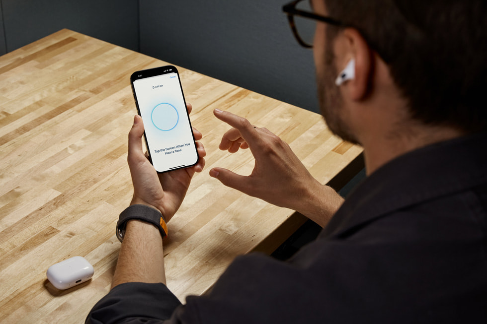 Uživatel sluchátek AirPods Pro 2 drží iPhone, na kterém používá funkci Sluchový test.