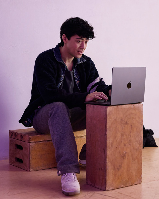 Kyle Hanagami sitter på en kasse i et studio og skriver på en MacBook Pro som står på en annen kasse.