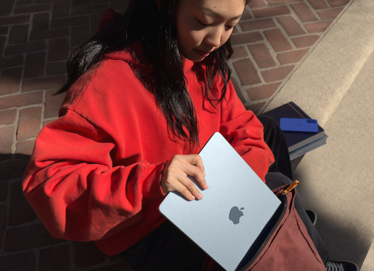 Une personne assise sur des escaliers en pierre range un MacBook dans un sac à dos.