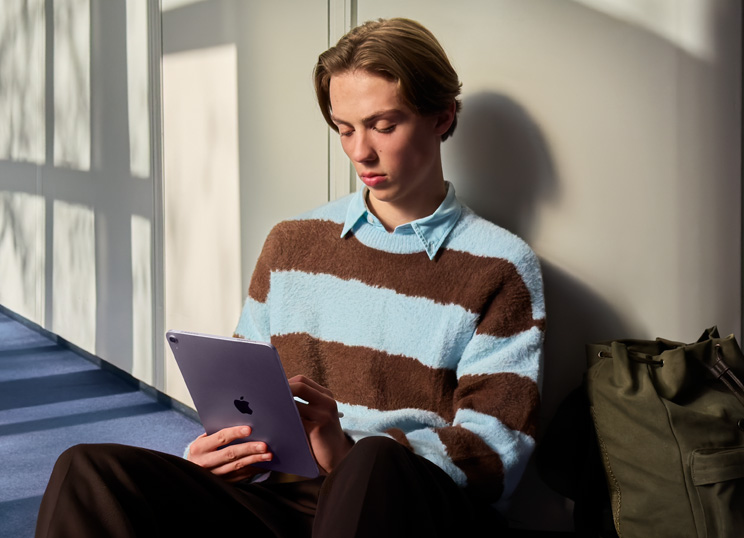 Une personne assise par terre dans une pièce lumineuse utilise un iPad et un Apple Pencil.