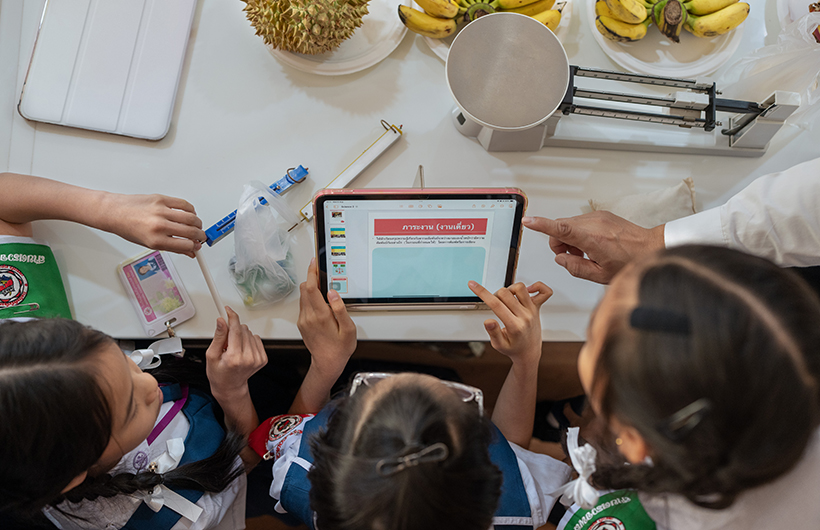 Autour d’un iPad, trois élèves du primaire collaborent à une présentation dans le cadre d’un projet de sciences.