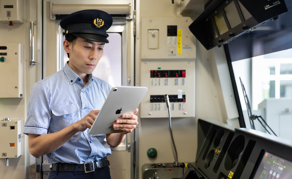 運転士が、自身の運行する車両の明るい運転室で、iPadを操作しながら業務を行っている