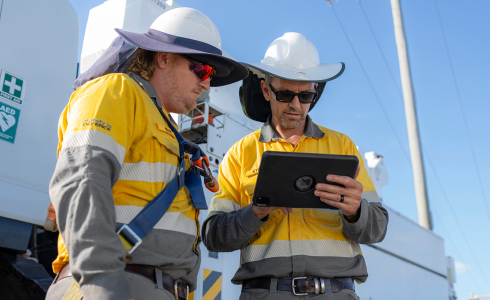 Dos trabajadores colaboran en un iPad mientras están de pie junto a un camión de servicios públicos