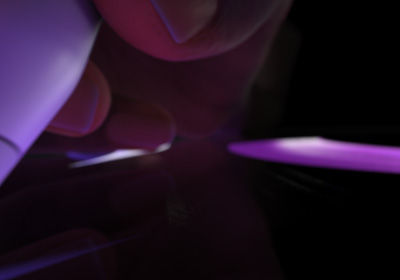 Ruka drží ceruzku Apple Pencil Pro v polohe pripravenej na písanie. Hrot sa dotýka displeja a kreslí hrubé, žiarivo fialové ťahy.