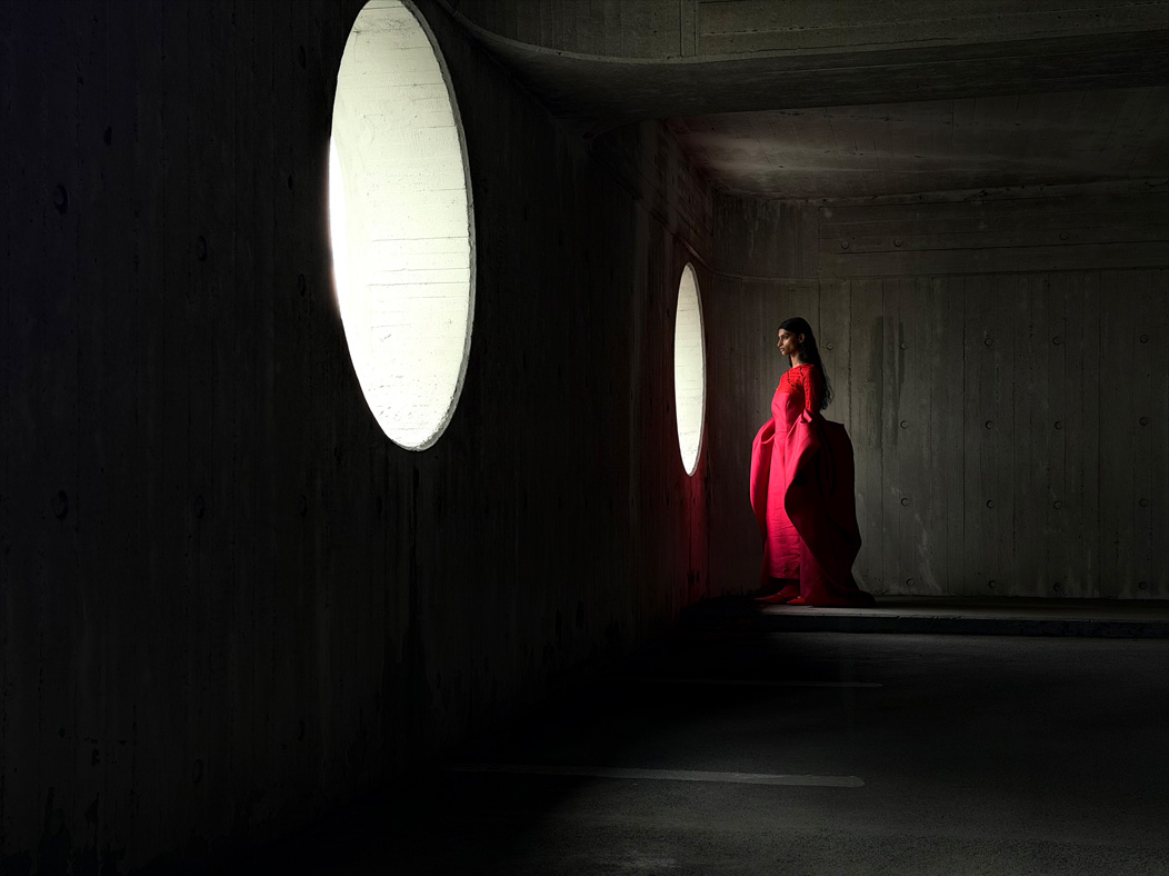 Une femme vêtue d’une longue robe rouge se fait photographier dans une pièce vide. L’app Appareil photo change de distance focale pour illustrer les capacités du système caméra pro, mettant en valeur: 48 mm